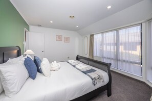 A hotel room with a bed, pillows, a bedside lamp, a window with curtains, and two framed pictures on the wall.