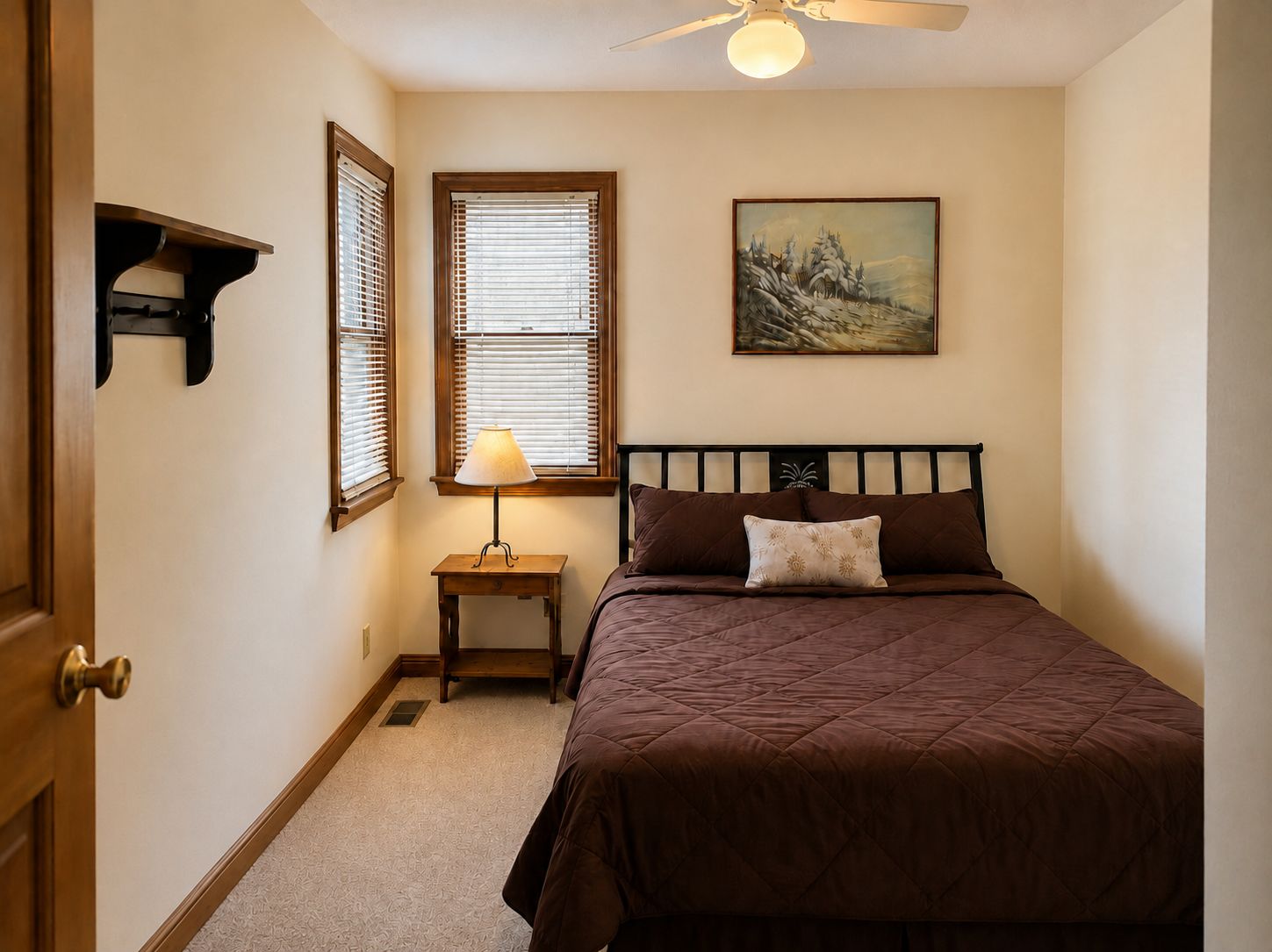 Une chambre à coucher avec un lit, une table de chevet, une lampe, un tableau et un ventilateur de plafond.