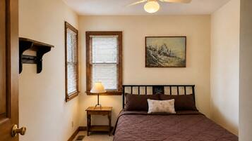 Une chambre à coucher avec un lit, une table de chevet, une lampe, un tableau et un ventilateur de plafond.