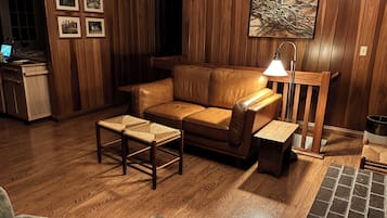 Una sala acogedora con un sofá de cuero, una mesa de centro de madera y un banco. Hay un cuadro en la pared y una lámpara sobre una mesita.