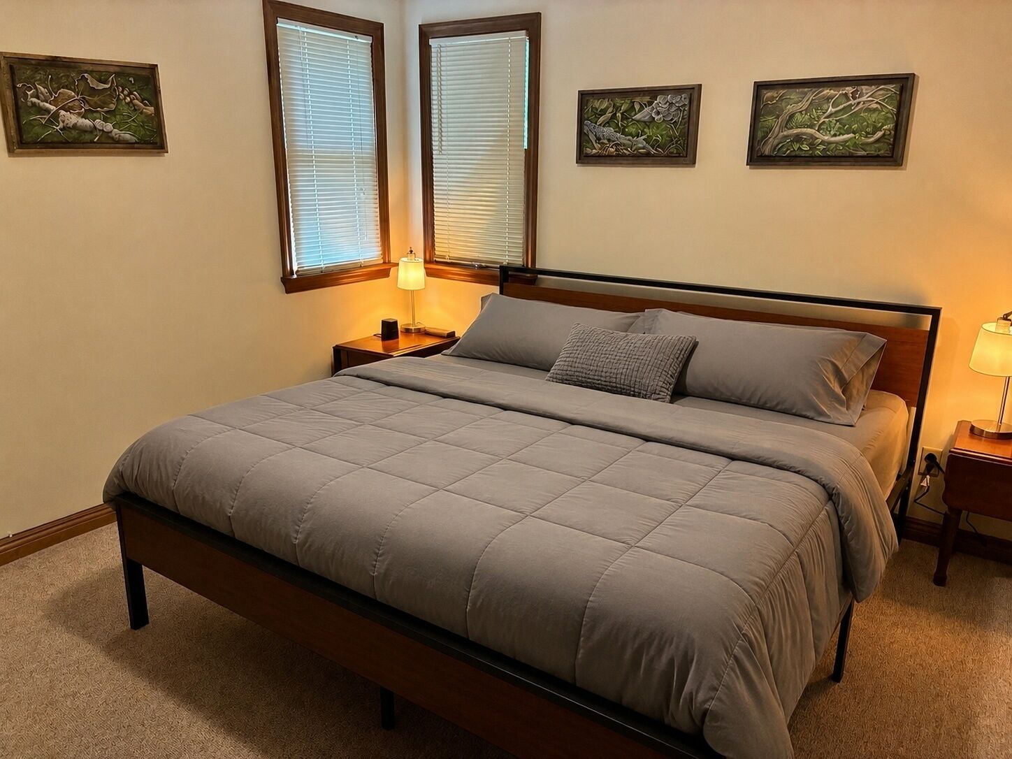 Une chambre à coucher avec un lit, deux tables de chevet, une lampe et trois œuvres d’art encadrées accrochées au mur.