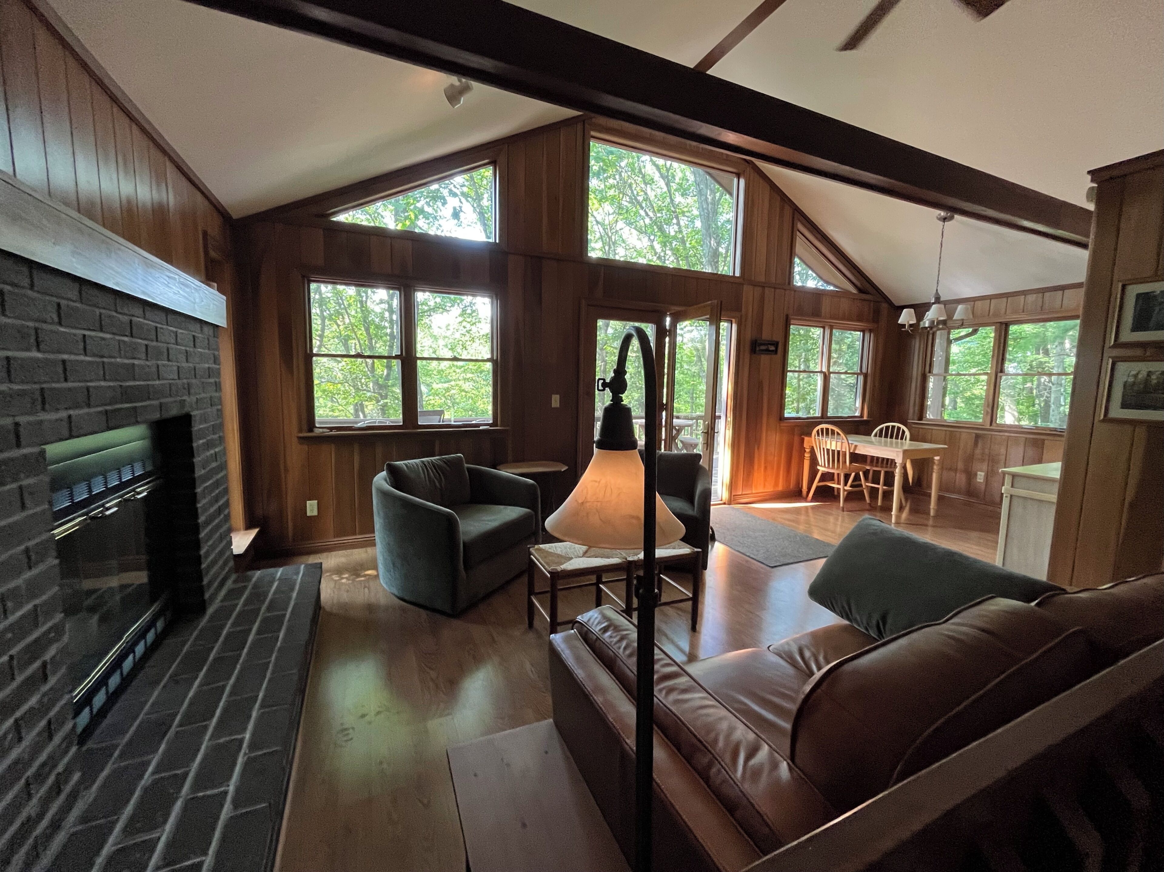 A cozy cabin interior with a fireplace, seating area, and large windows offering natural light.