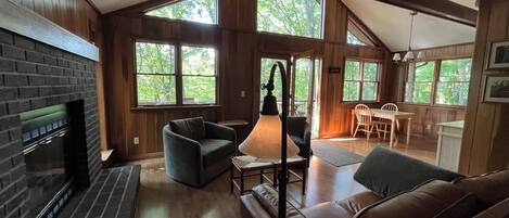 A cozy cabin interior with a fireplace, seating area, and large windows offering natural light.