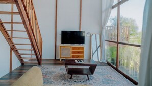 Quarto com escada de madeira, televisão de tela plana em um armário de madeira, tapete estampado e uma grande janela com vista para o verde.
