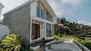 Uma casa moderna de dois andares com fachada de pedra, janelas amplas e uma escadaria de pedra que leva à entrada.