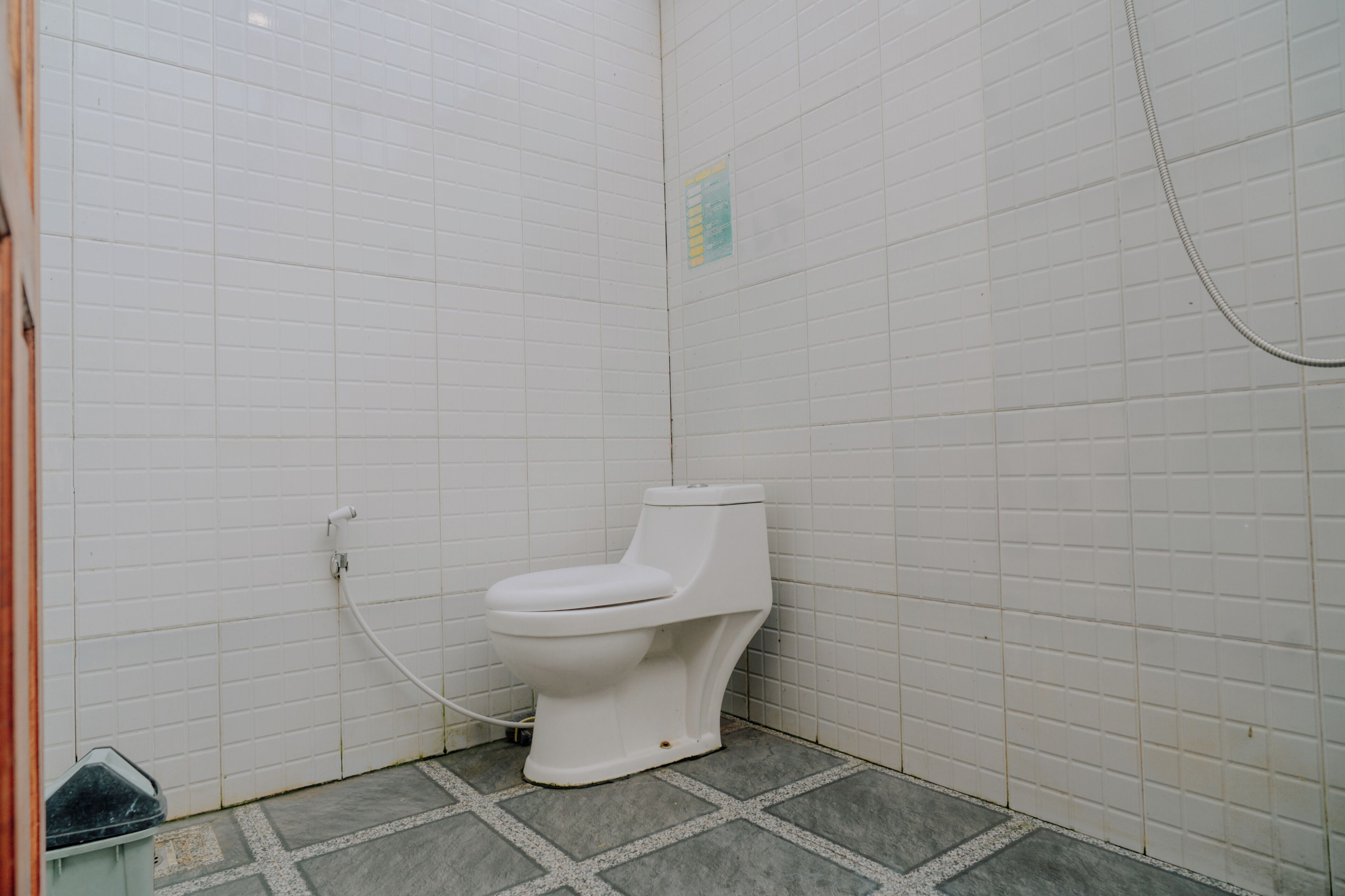 Een kleine, afgesloten badkamer met witte betegelde wanden en een witte toilet.