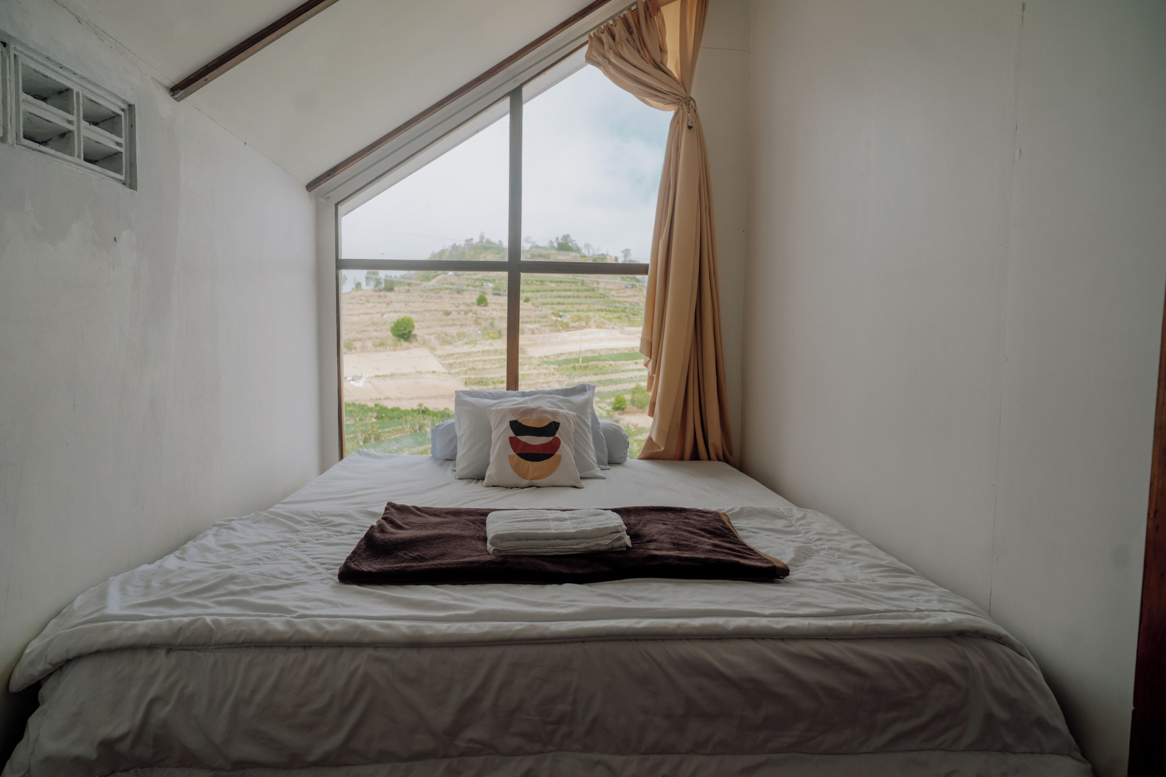 A single bed with a view of a rural landscape through a large window.
