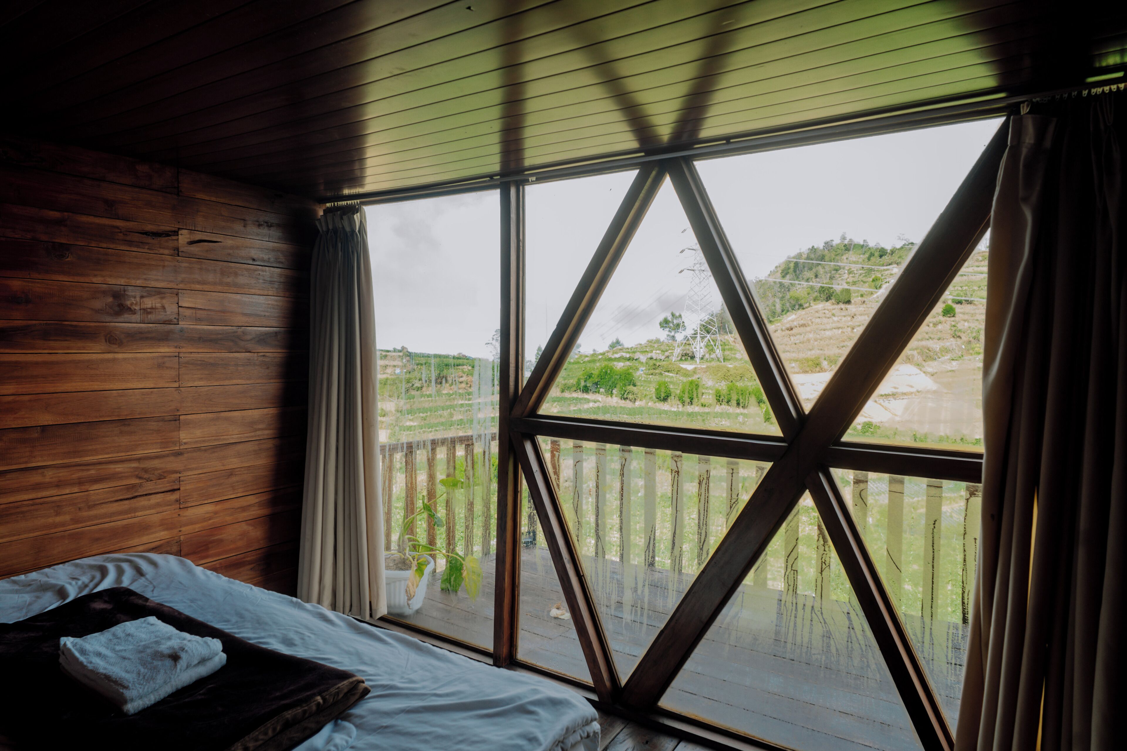 A room with a bed, wooden walls, and a large window with a view of a landscape.