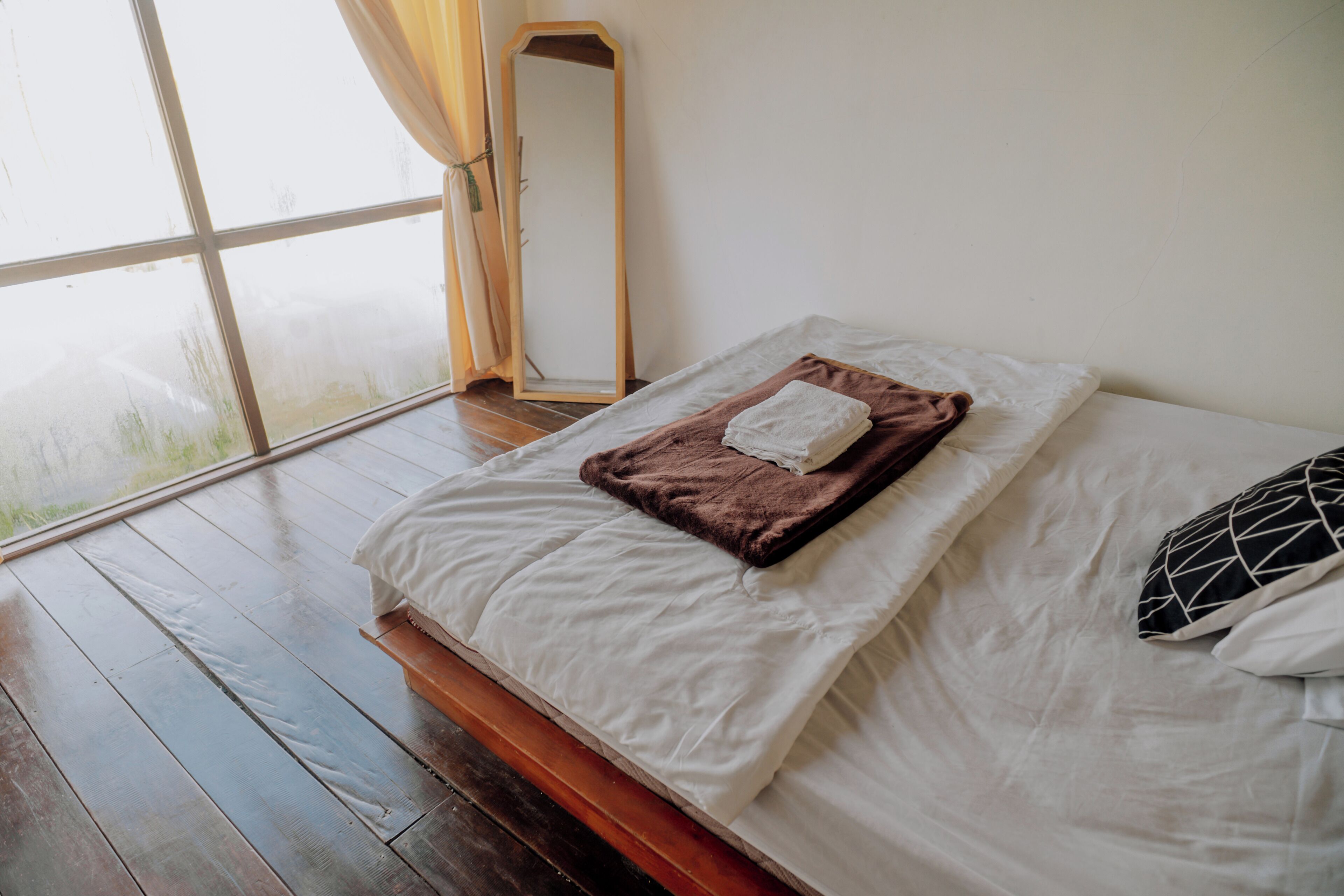 Une chambre à coucher avec un lit, un plancher en bois, une fenêtre avec des rideaux et un miroir.
