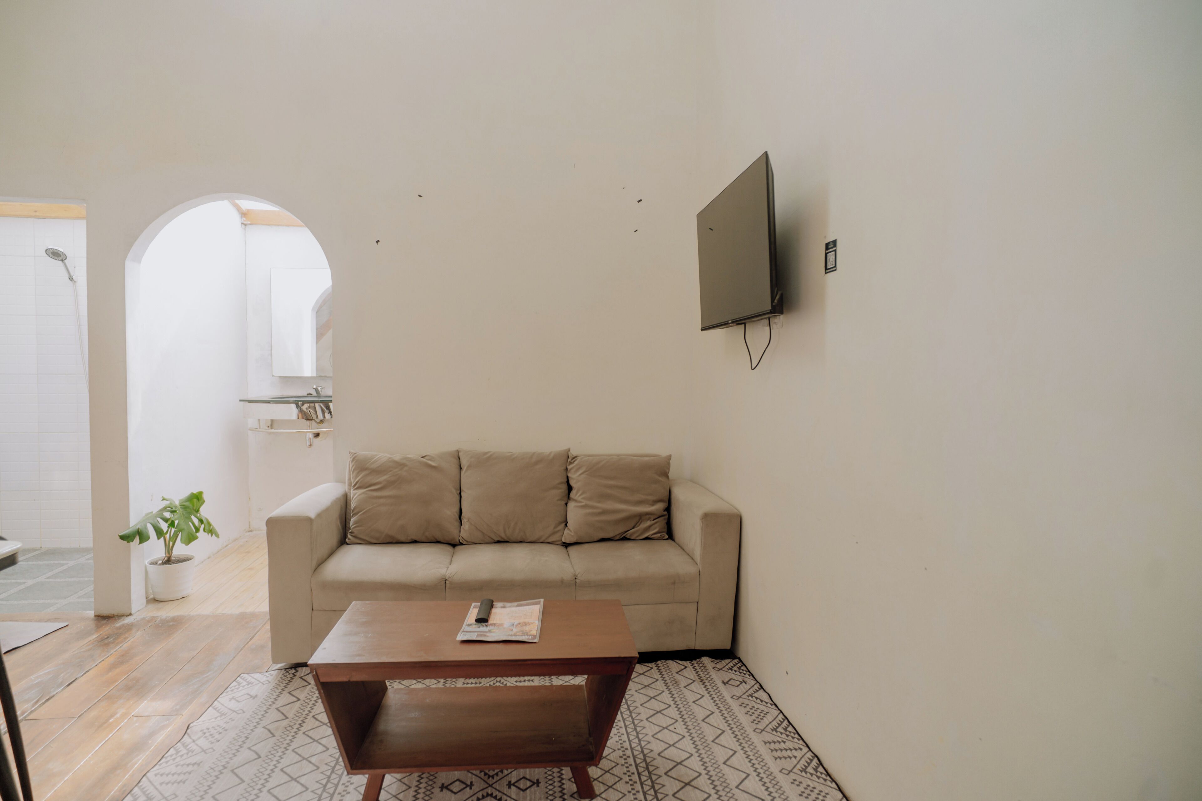 A living room with a beige sofa, a wooden coffee table, and a flat-screen TV mounted on the wall.