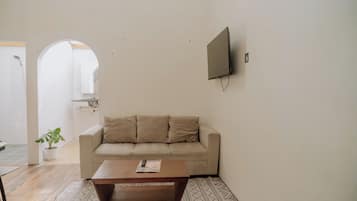 A living room with a beige sofa, a wooden coffee table, and a flat-screen TV mounted on the wall.