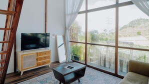 Um quarto com uma janela grande, uma televisão sobre um armário de madeira, um sofá e um tapete estampado.