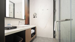Un baño moderno con cabina de ducha de vidrio, un salpicadero de mármol blanco y un mueble de tocador de madera.