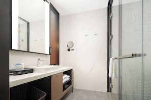 A modern bathroom with a glass shower enclosure, a white marble backsplash, and a wooden vanity.