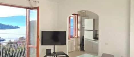 Una sala de estar moderna con un televisor grande, un comedor con mesa de vidrio y un balcón con vistas.