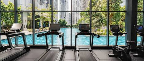 A gym with treadmills and exercise equipment, overlooking a swimming pool and high-rise buildings.