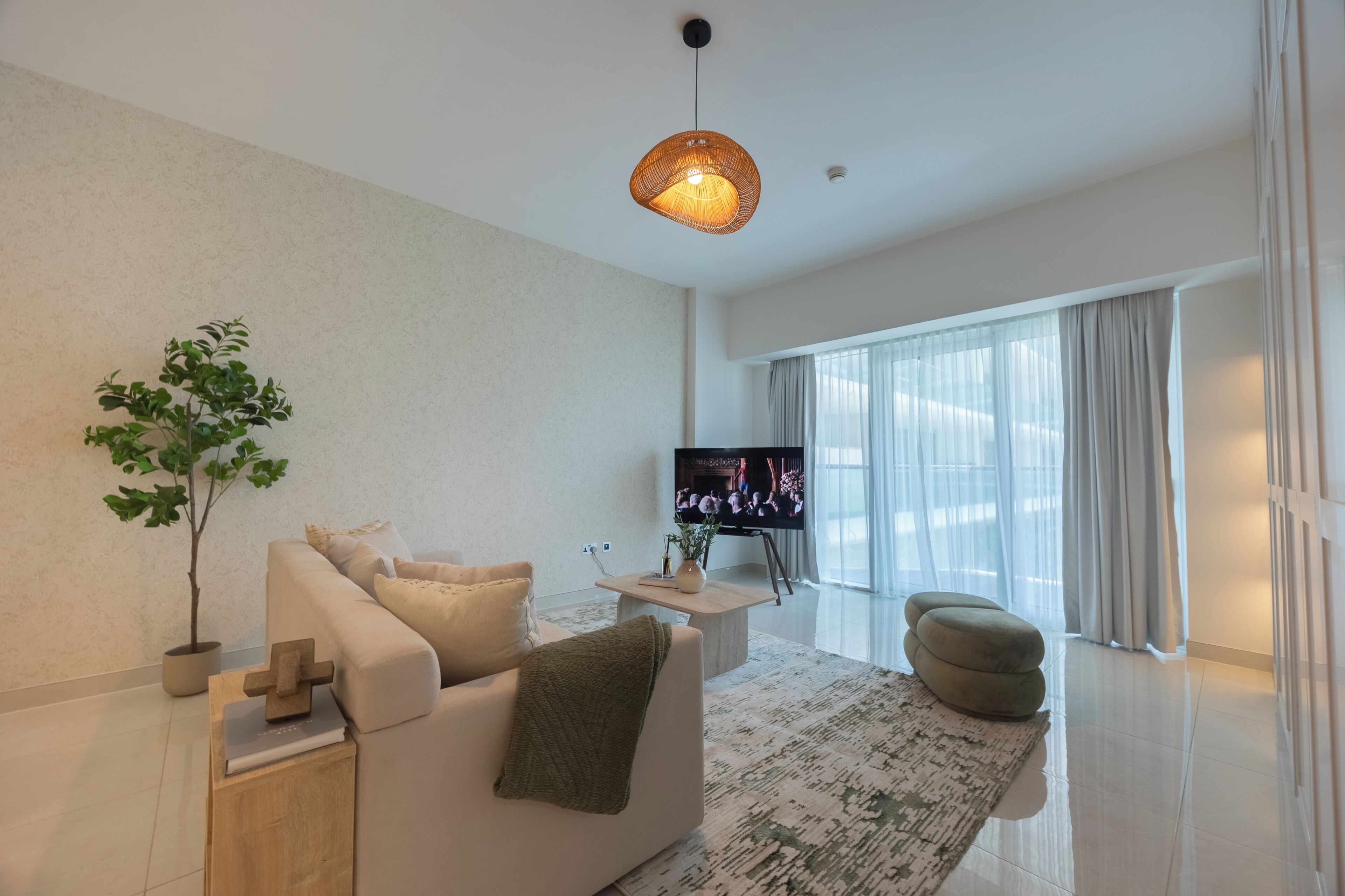 Un salon moderne avec un canapé, une table basse, un téléviseur et une grande fenêtre avec des rideaux.