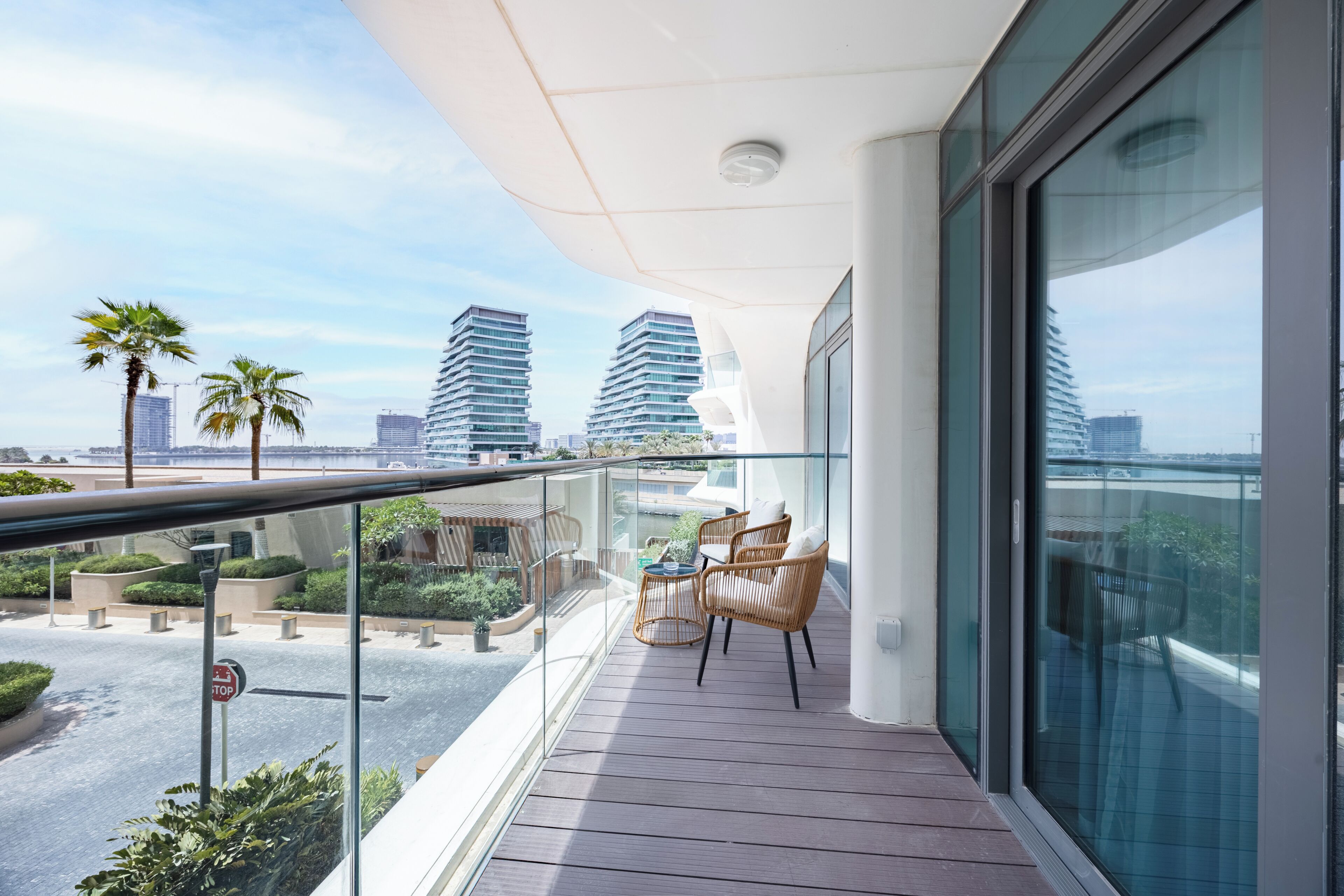 Un balcon doté d'une balustrade en verre, de meubles en osier et offrant une vue sur les immeubles de grande hauteur.