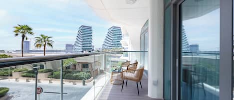 A balcony with a glass railing, wicker furniture, and a view of high-rise buildings.
