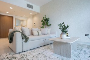 A modern living room with a sofa, a coffee table, a plant, and a mirror. - Bloomfields 1BR in Al Hadeel East (Abu Dhabi)