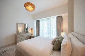 A modern bedroom with a large bed, a dresser, a mirror, and a hanging light fixture. - Bloomfields 1BR in Al Hadeel East (Abu Dhabi)