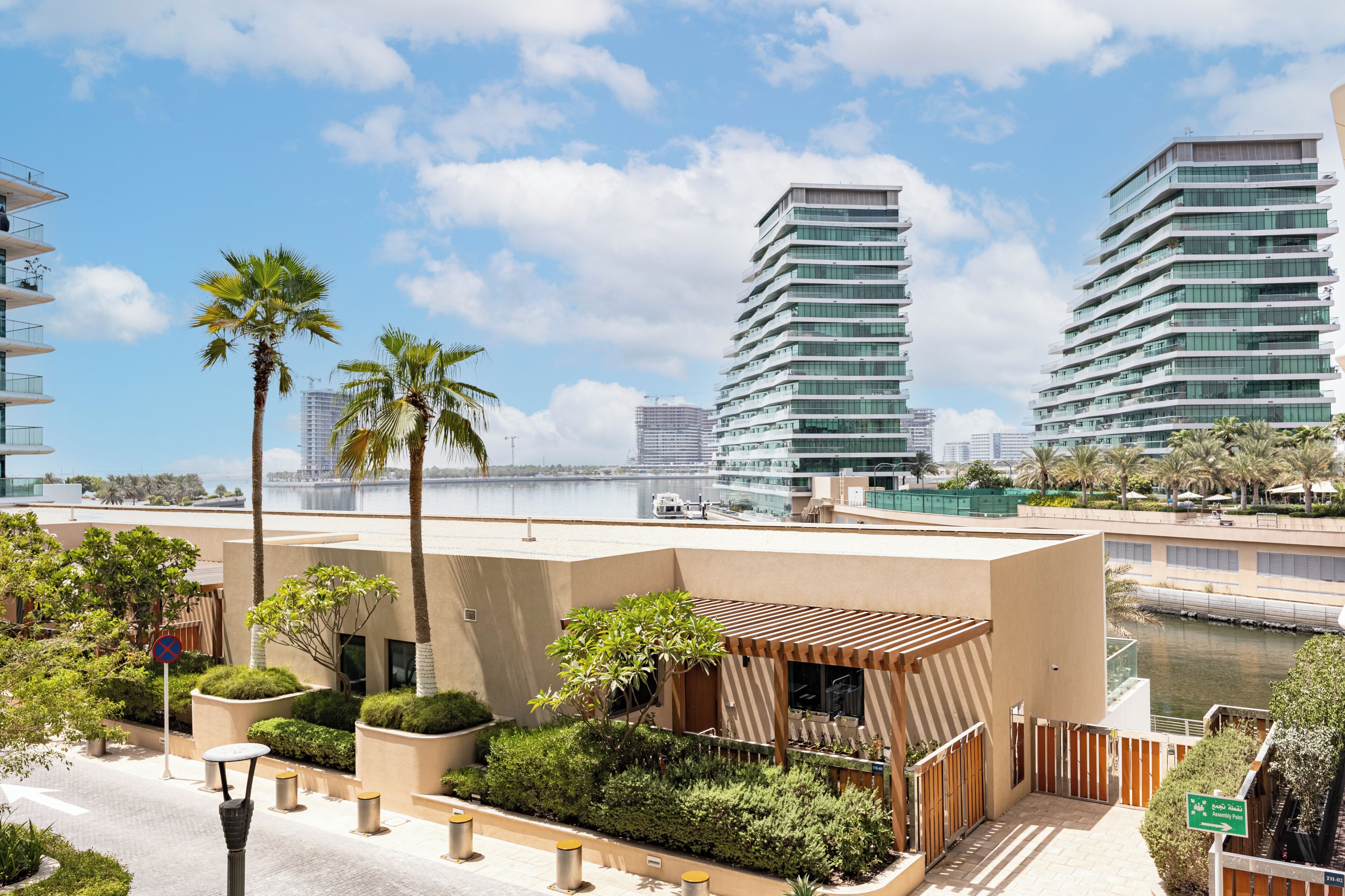 A modern building with a flat roof, surrounded by palm trees and a body of water.