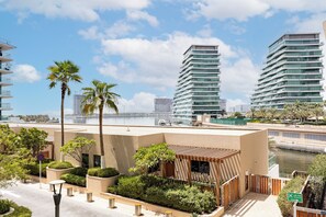 A modern building with a flat roof, surrounded by palm trees and a body of water. - Bloomfields 1BR in Al Hadeel East (Abu Dhabi)