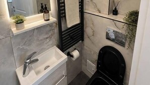 Ein modernes Badezimmer mit Marmorwand, einem schwarzen Handtuchhalter, einem weißen Waschbecken und einer schwarzen Toilette.