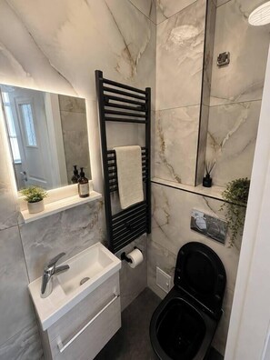 Ein modernes Badezimmer mit Marmorwand, einem schwarzen Handtuchhalter, einem weißen Waschbecken und einer schwarzen Toilette.