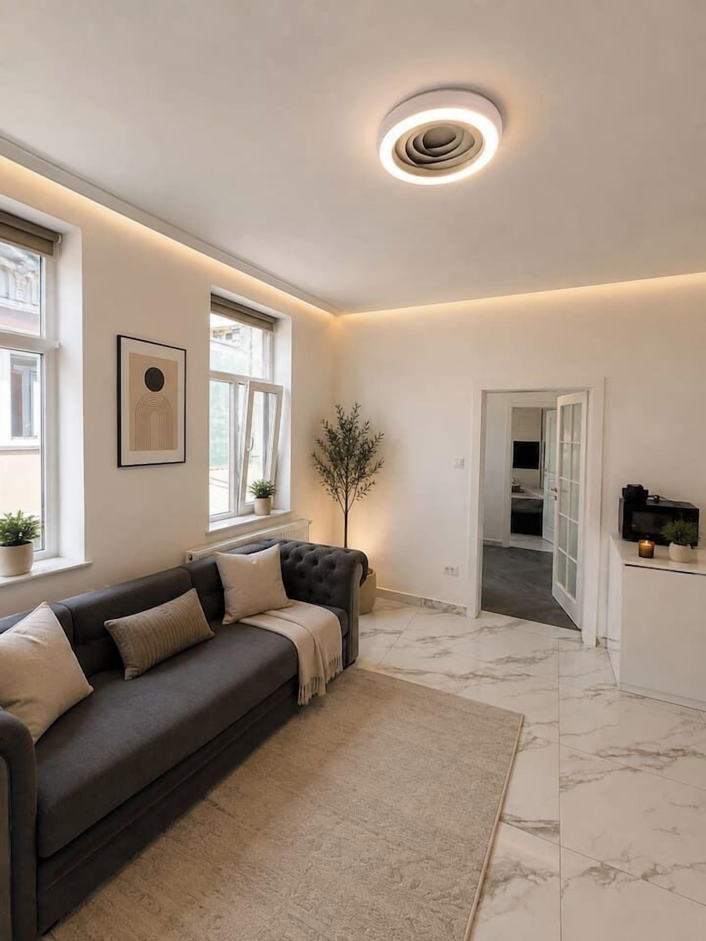 A modern living room with a dark grey sofa, a white rug, and a ceiling light fixture.