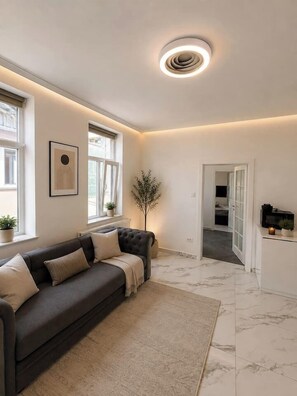 Ein modernes Wohnzimmer mit einem dunkelgrauen Sofa, einem weißen Teppich und einer Deckenleuchte.