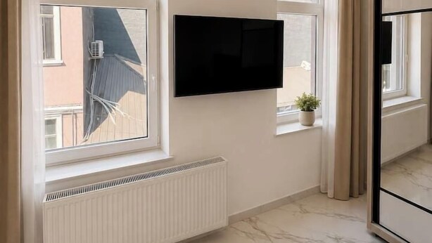 Ein modernes Hotelzimmer mit großem Fenster, einem flachbildfernseher an der Wand und einer Heizung unter dem Fenster.