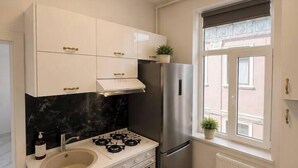 Eine kompakte Küche mit weißen Schränken, einem Edelstahl-Kühlschrank, einem Gasherd und einem Fenster mit Blick.