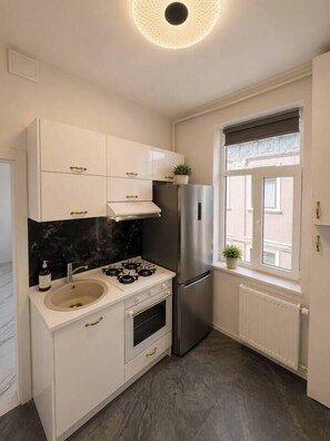 Eine kompakte Küche mit weißen Schränken, einem Edelstahl-Kühlschrank, einem Gasherd und einem Fenster mit Blick.