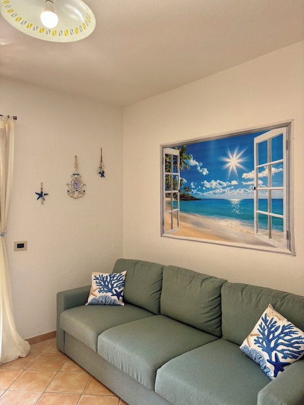 Ein Zimmer mit einem grünen Sofa, einer Wanduhr und einem Wandbild mit Strandmotiv.