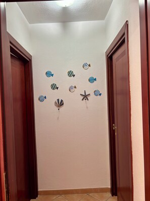 A hallway with two wooden doors, a textured wall, and decorative fish and starfish wall art.