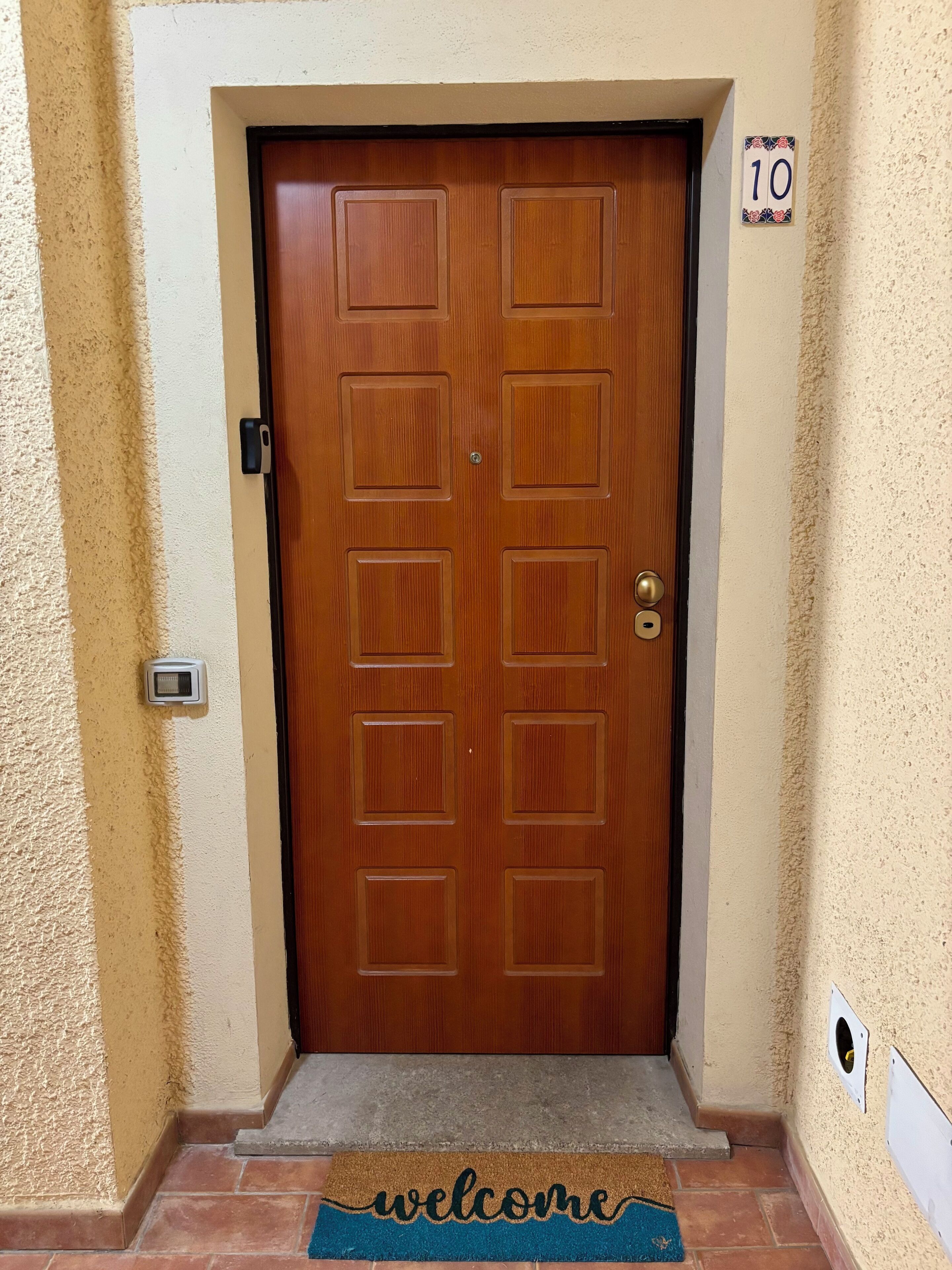 Une porte double en bois, avec un paillasson sur lequel est écrit « bienvenue » et une plaque indiquant le numéro 10.