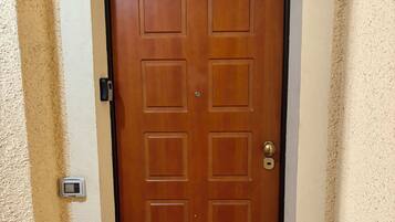 Une porte double en bois, avec un paillasson sur lequel est écrit « bienvenue » et une plaque indiquant le numéro 10.