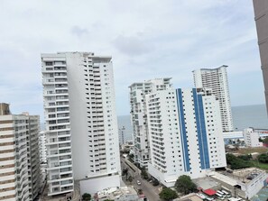 A high-rise residential building with multiple balconies, a parking area, and a view of the sea.
