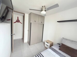 A bedroom with a bed, a wardrobe, a ceiling fan, and a TV mounted on the wall.