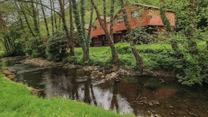 A red cabin with a river in front, surrounded by trees and greenery. - Cabin No. 4 - Salt and Fern Cabins (Port Talbot)