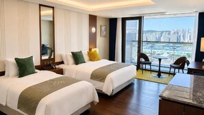 Habitación de hotel con dos camas, zona de comedor y vistas a un paisaje urbano.