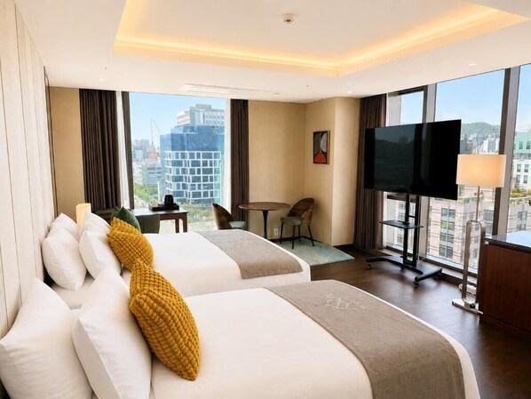 A hotel room with two beds, a TV, a desk, and a view of the city. - westernpalace (Incheon)