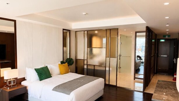 A modern hotel room with a large bed, a nightstand, a desk, and a sliding door leading to a bathroom.