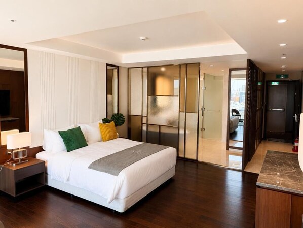 A modern hotel room with a large bed, a nightstand, a desk, and a sliding door leading to a bathroom.