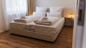 A neatly made bed with white linens and folded towels, a bedside table with a lamp, and a wooden floor. - Design apartment by the park with parking (Celle)