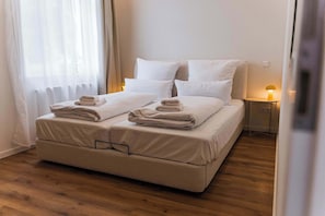 A neatly made bed with white linens and folded towels, a bedside table with a lamp, and a wooden floor. - Design apartment by the park with parking (Celle)