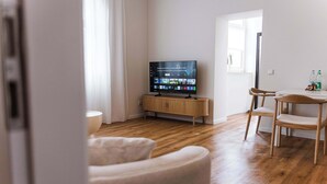 A modern living room with a flat-screen TV on a wooden stand, a dining area with a table and chairs, and a large window providing natural light. - Design apartment by the park with parking (Celle)