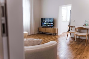 A modern living room with a flat-screen TV on a wooden stand, a dining area with a table and chairs, and a large window providing natural light. - Design apartment by the park with parking (Celle)