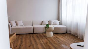 Ein stilvolles Wohnzimmer mit einer gebogenen Couch, einem runden Couchtisch mit Pflanze und Holzböden.